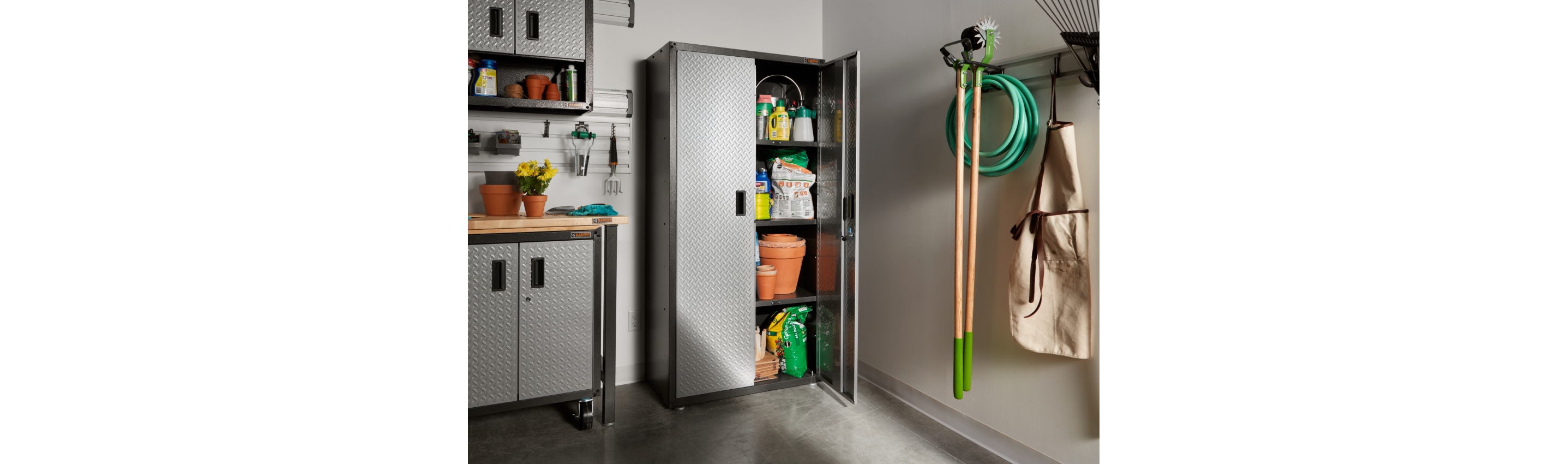 An opened Gladiator unit in a garage, holding various gardening supplies. There are two more Gladiator Modular Cabinets with plants on top, and a GearTrack System holding gardening tools and a garden hose. Gardening tools hang on the wall above one of the cabinets.