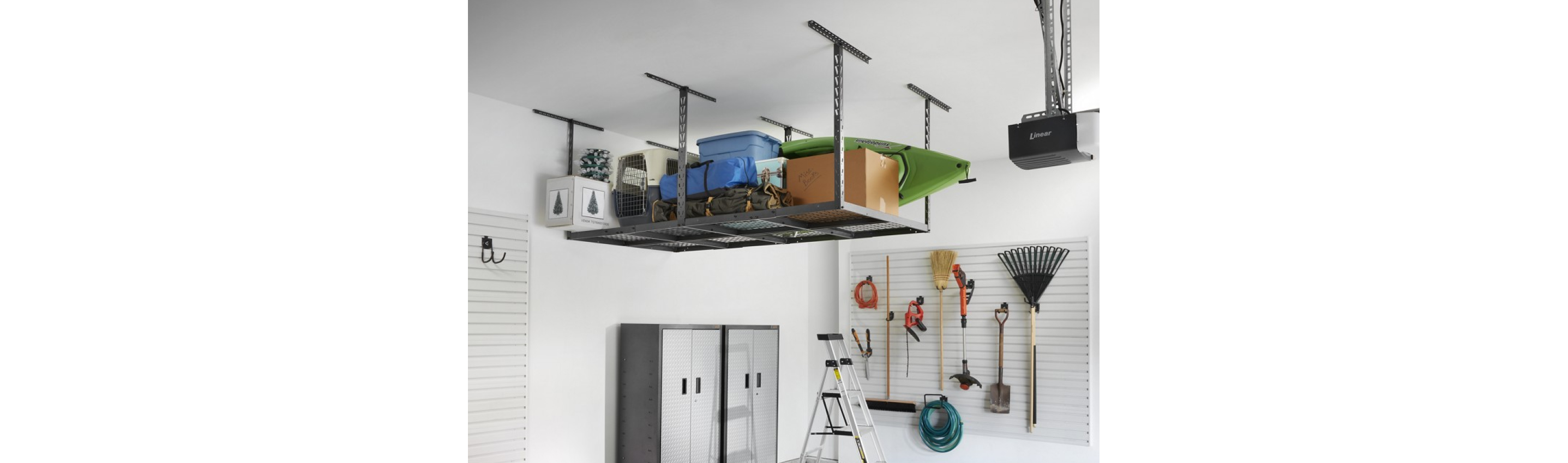 A garage with Gladiator Overhead Storage holding a box, kayak, bags, bins and more. There's also a Gladiator GearBox, ladder and gardening tools hanging on the wall on Gladiator Hooks. 