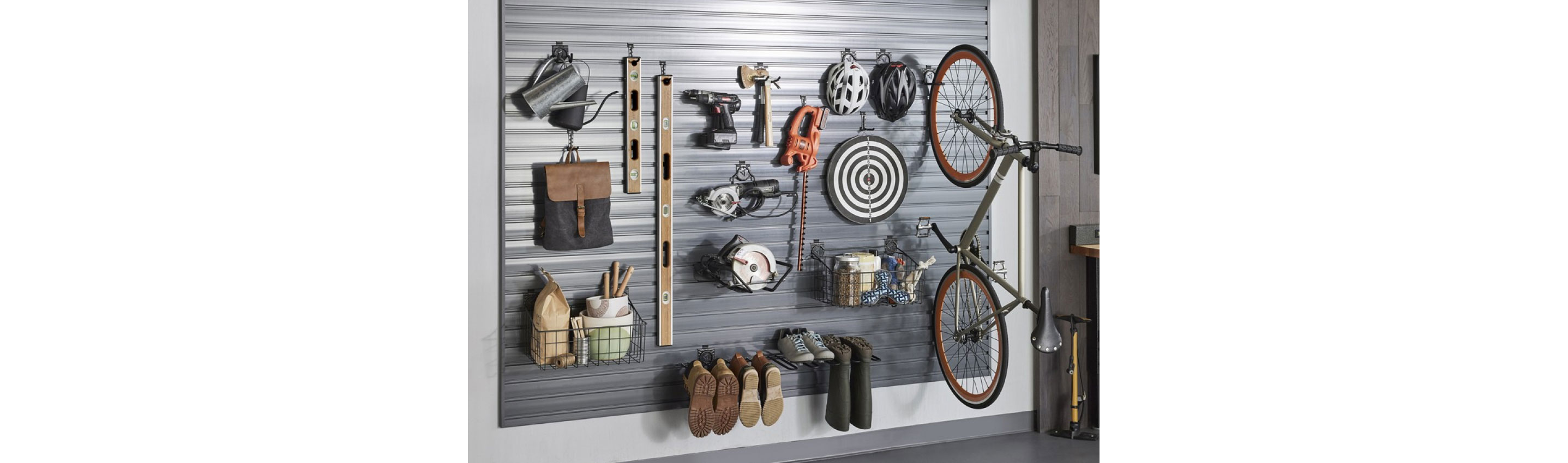 Hanging on Gladiator Hooks on a wall are a watering can, a satchel, levels, a drill, saws, bicycle helmets, a bicycle, boots, shoes, rainboots and more.