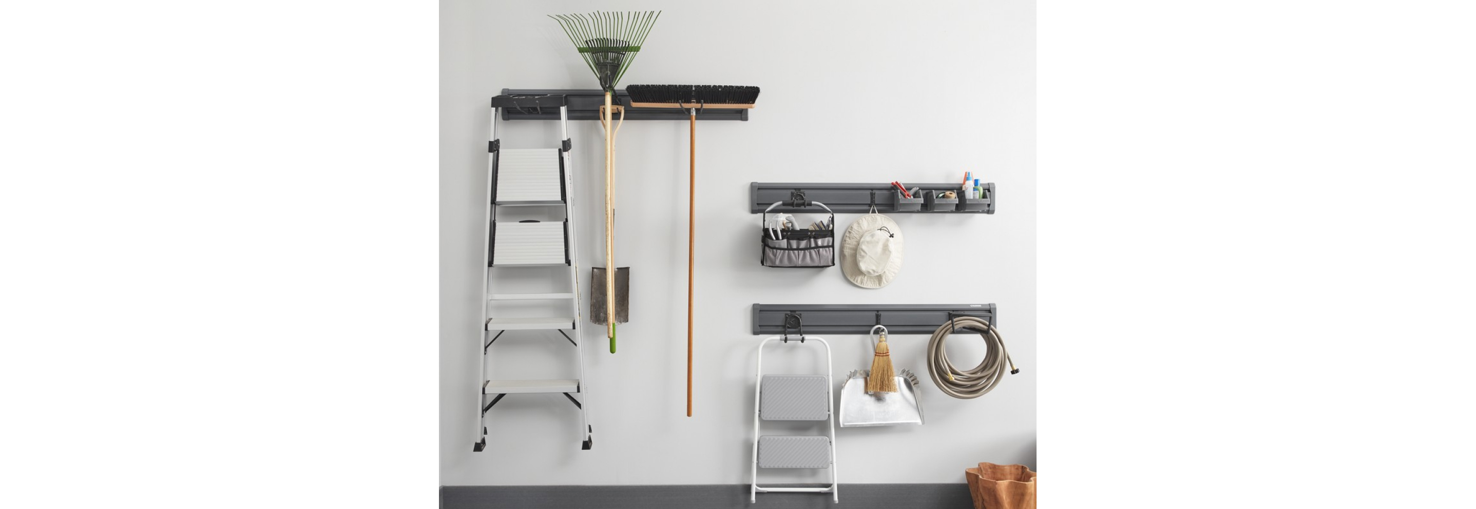 Hanging on three Gladiator Wall Systems are a ladder, rake, broom, hat, items in baskets, step stool, broom and dust pan and garden hose